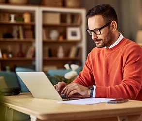 Man in orange sweater with laptop.